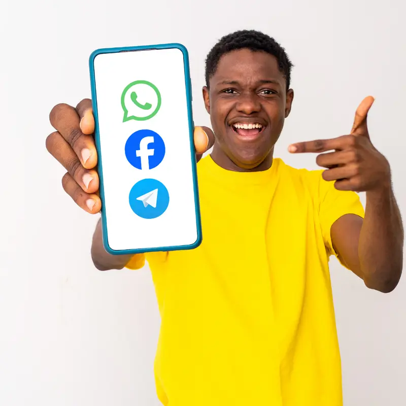 Smiling man holding up a phone showing WhatsApp, Facebook and Telegram logos