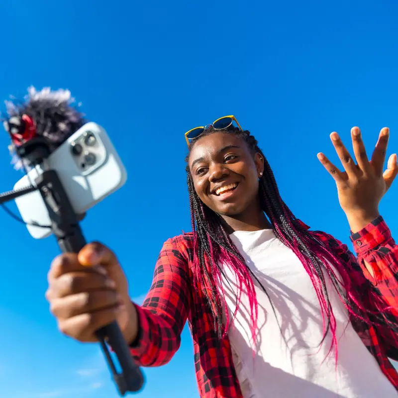 Content creator filming herself with a phone on a selfie stick