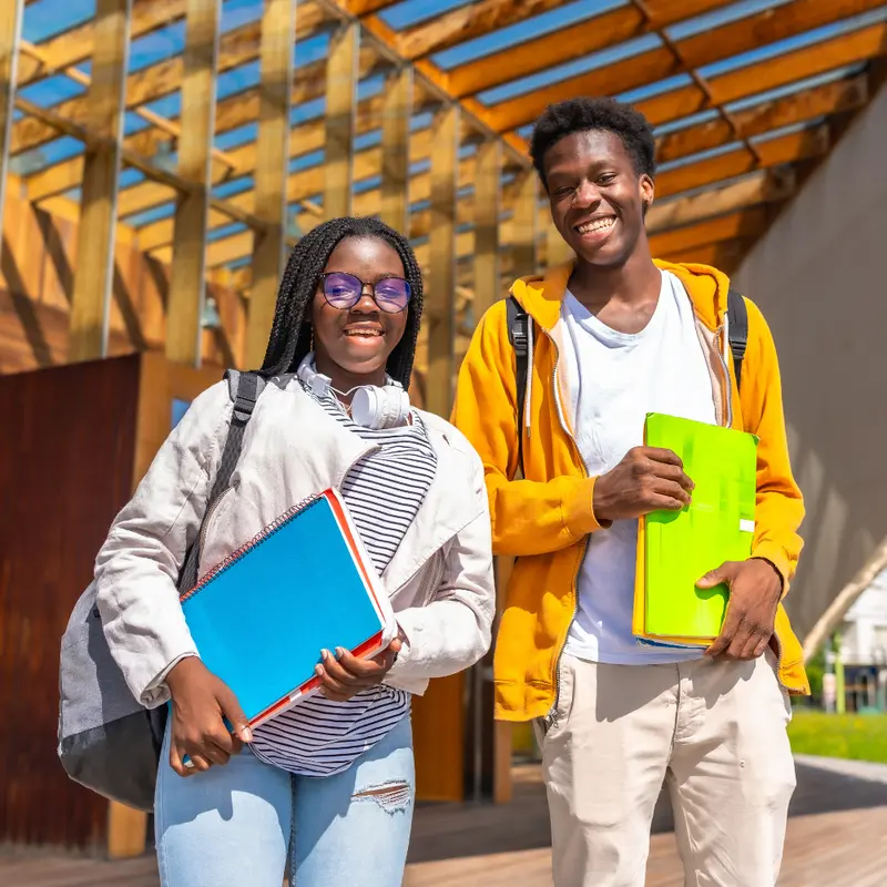 Two smiling students holding notebooks on campus